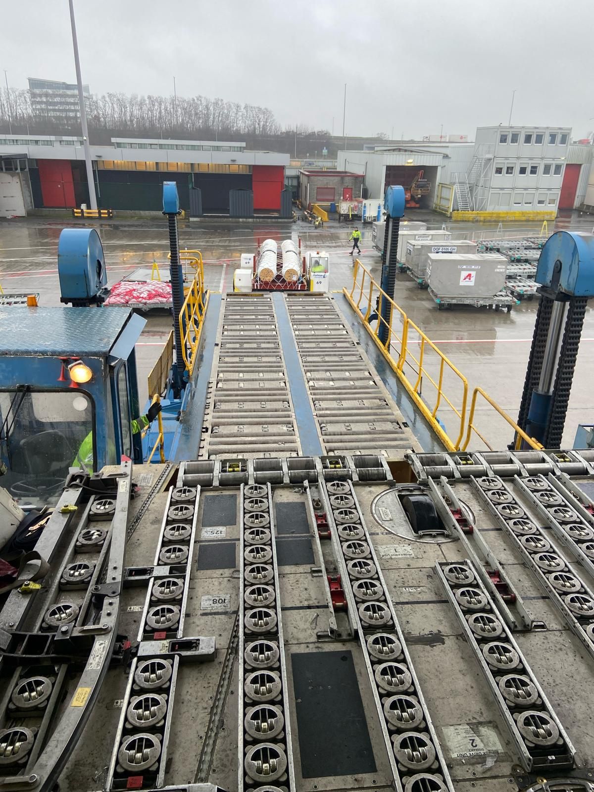 The empty roller-bed floor of a cargo aircraft main deck, looking out through the open door towards the loading dock.