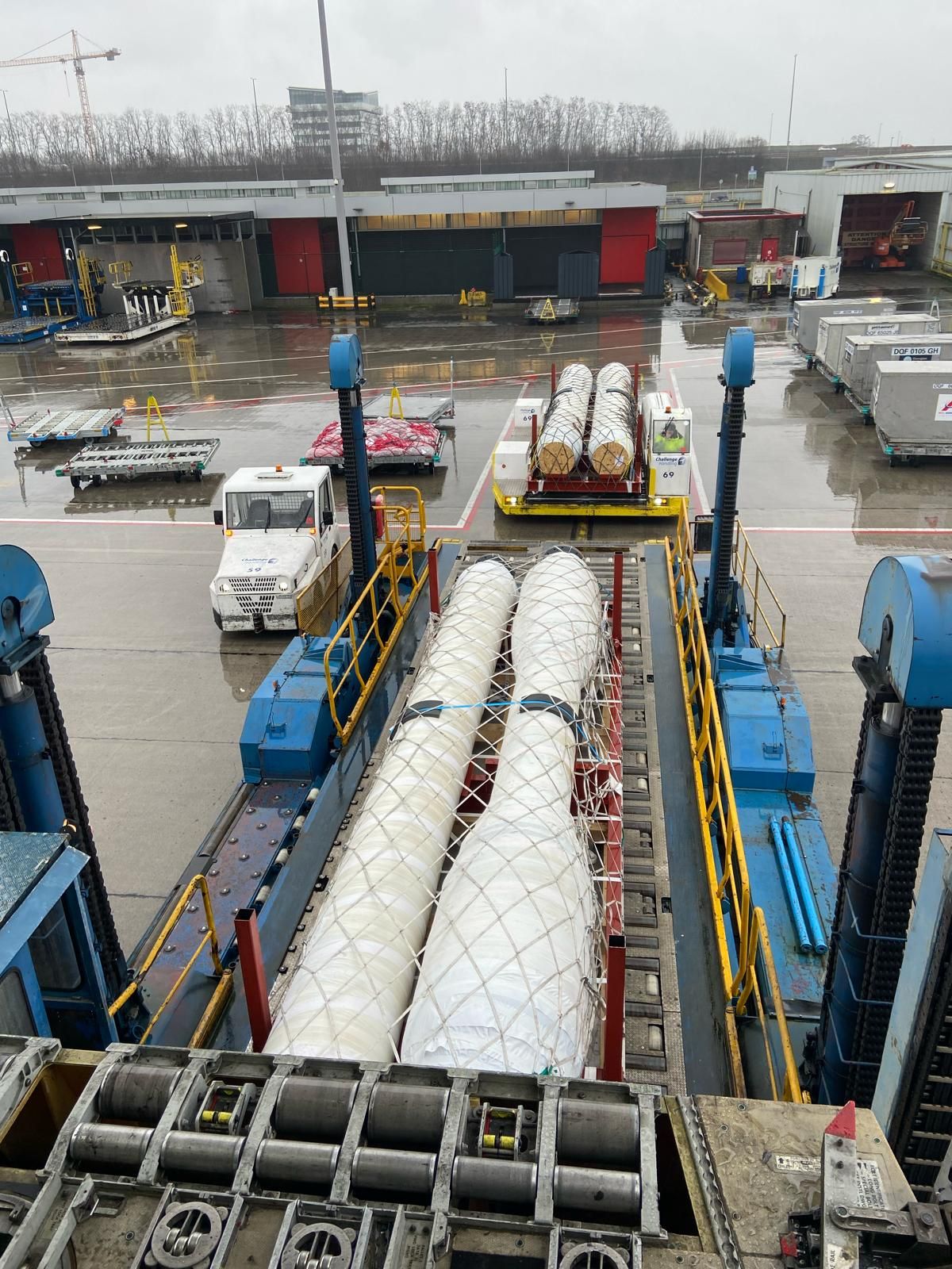 Wrapped tubing bundles on pallets at an airport cargo loading dock, waiting to be transferred to the aircraft.