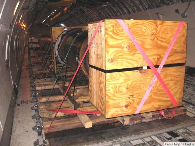 A timber case and a wrapped cylindrical item lashed with pink and black webbing to the roller floor inside the main deck of a cargo aircraft.