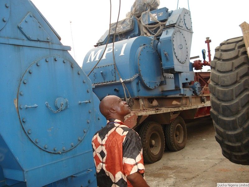 A man looking up at a large blue drilling pump unit loaded on a trailer beside a very large tyre.