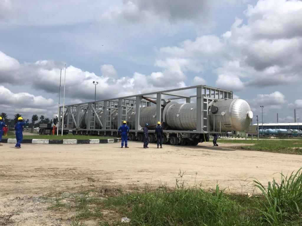 A module and pressure vessels on trailers on a site, with a group of workers in blue coveralls standing alongside.