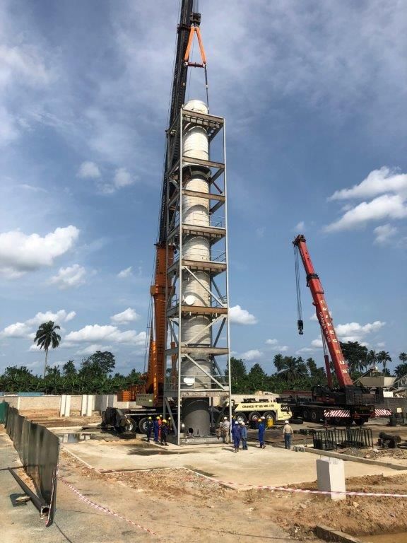 The tower being lowered onto its concrete foundation with crew in high-visibility clothing guiding it at the base.