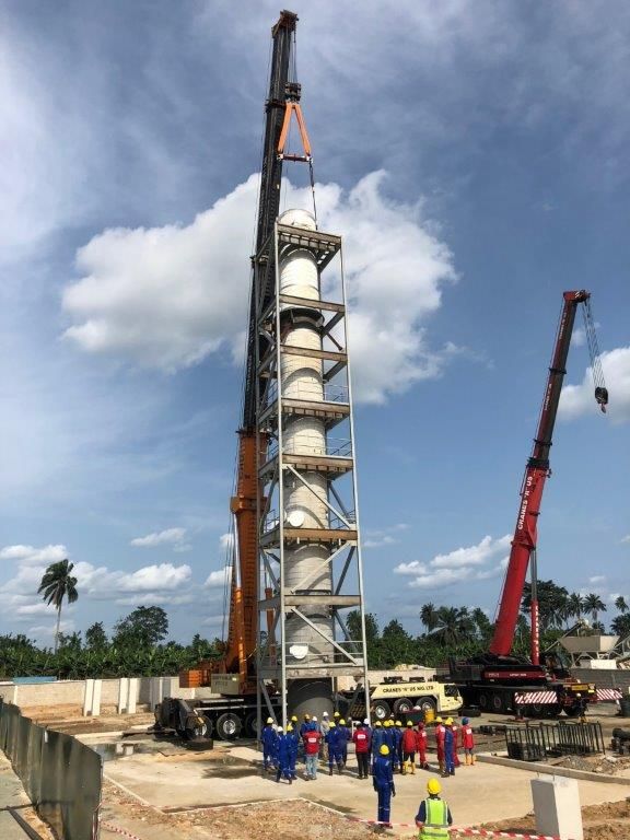 The process tower standing on its foundation with cranes still rigged and the ground crew gathered at the base.