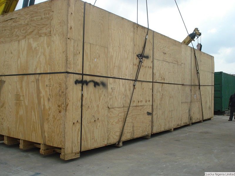 A large plywood-cased consignment slung on wire ropes ready for lifting, standing on a concrete apron.
