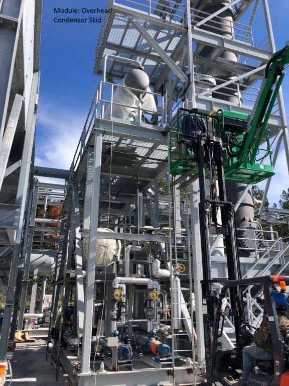 A tall overhead condenser skid with dense pipework and a green access platform alongside.