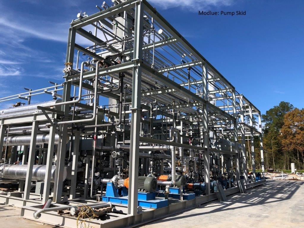 A large two-level pump skid with insulated pipework and blue pumps, under blue sky in a fabrication yard.