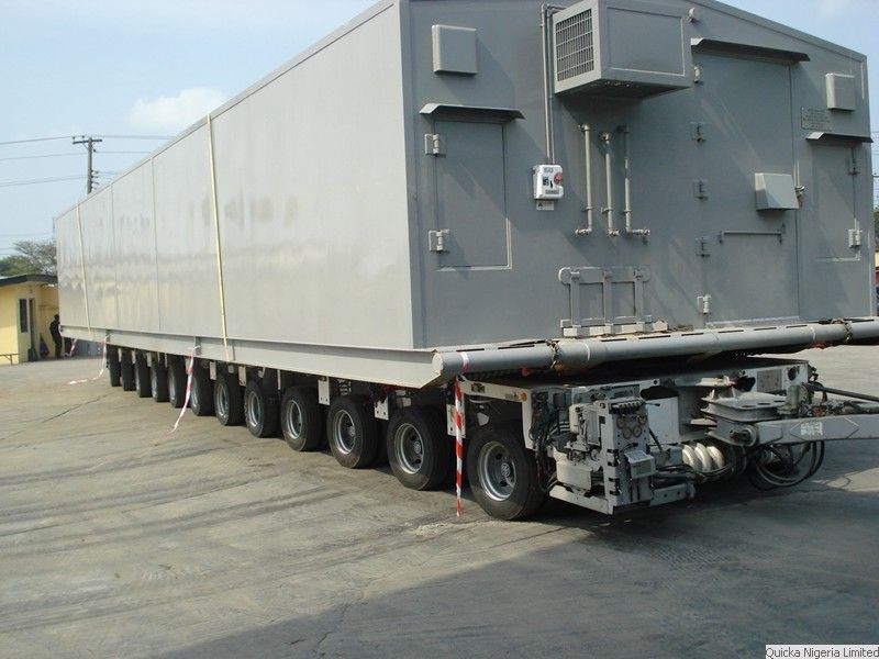 A long grey power module carried on a many-axled modular transporter, photographed along its length.