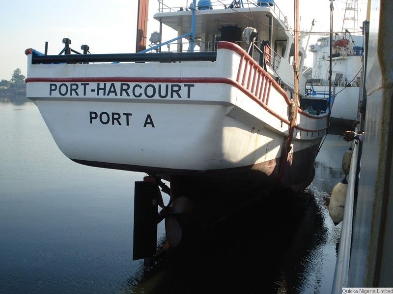 A workboat lettered PORT-HARCOURT PORT A afloat in calm water beside a larger vessel.