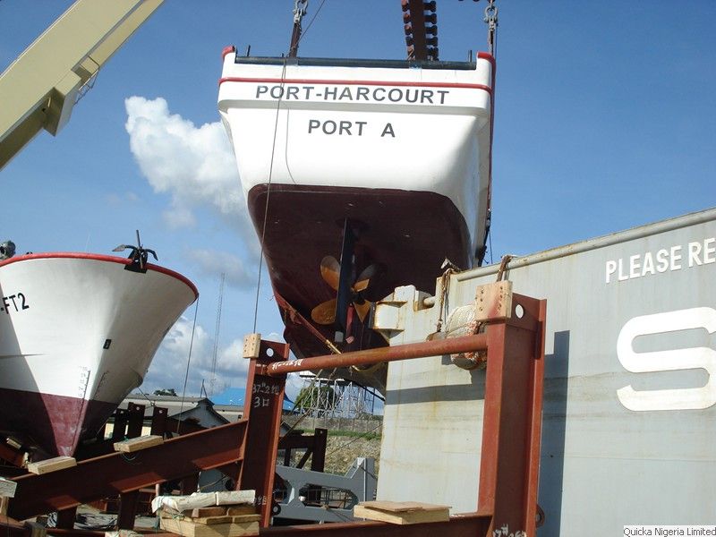 The bow of a workboat named PORT-HARCOURT PORT A suspended on slings during a lift, with a green vessel hull behind.